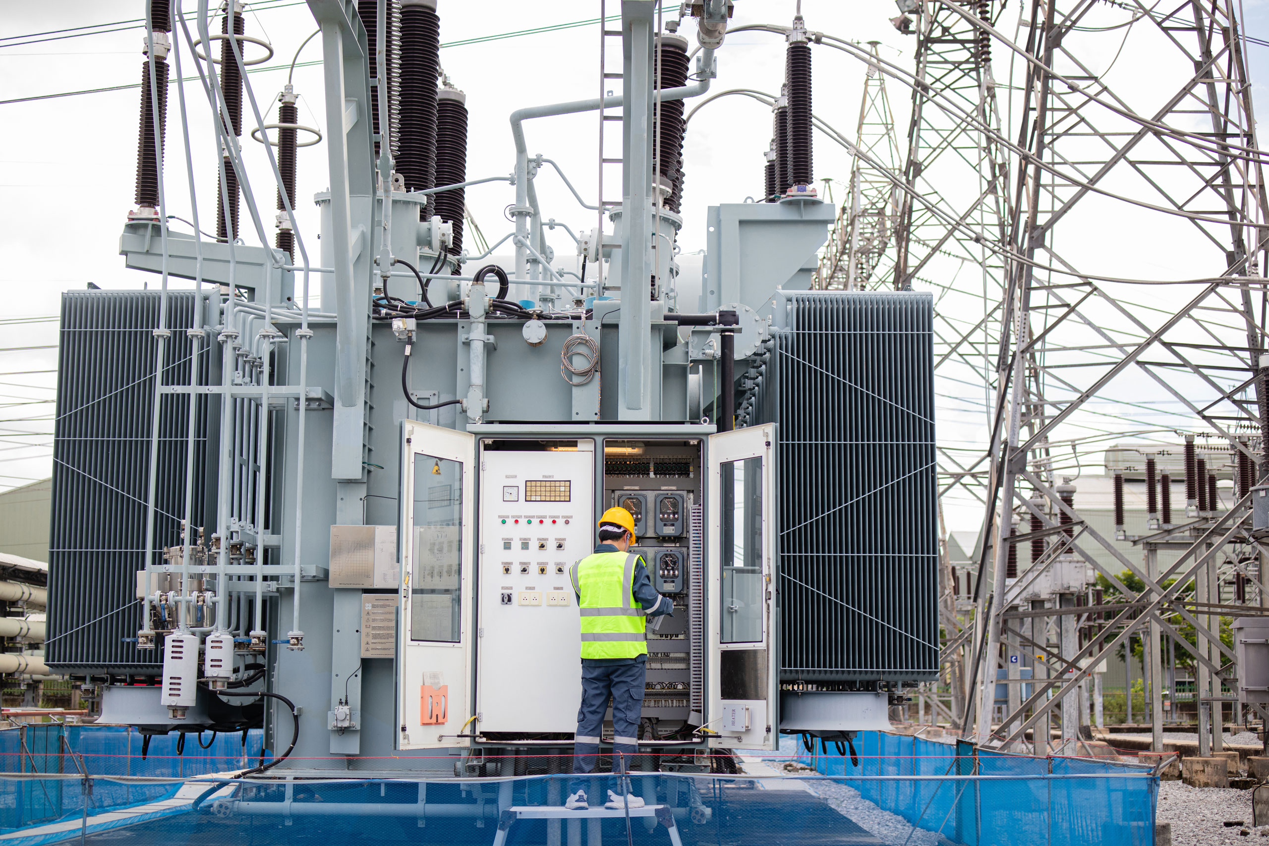 Engineer performs inspection on large transformer at electrical substation ensuring safety and functionality in industrial environment with power lines and equipment