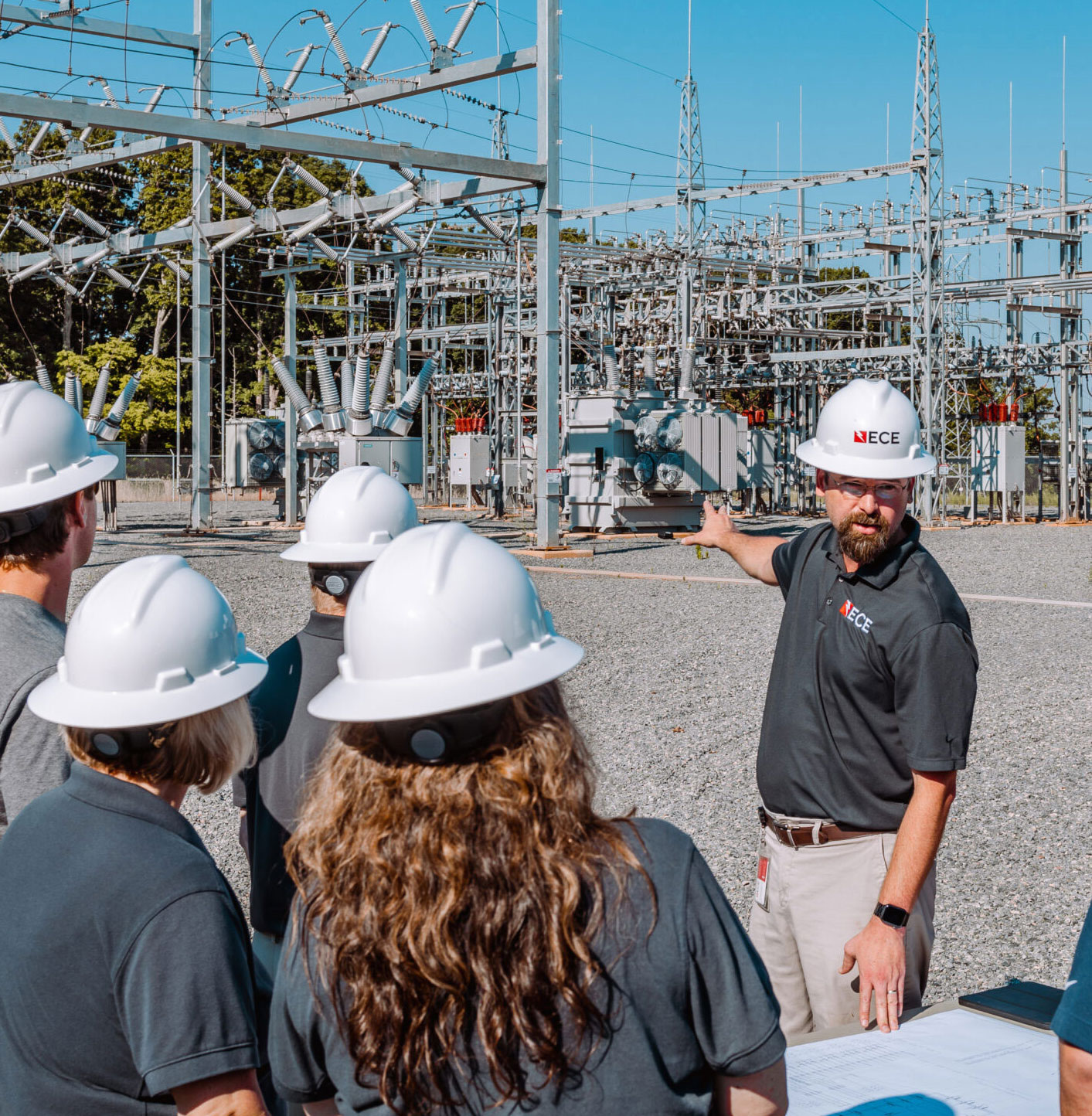 ECE team leader leading a meeting with a group of staff members in front of a substation